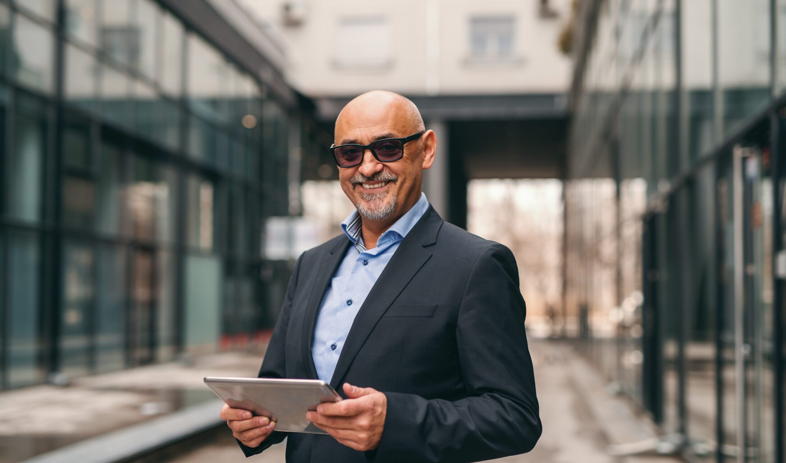smiling-bearded-senior-suit-holding-tablet-while-standing-outdoors
